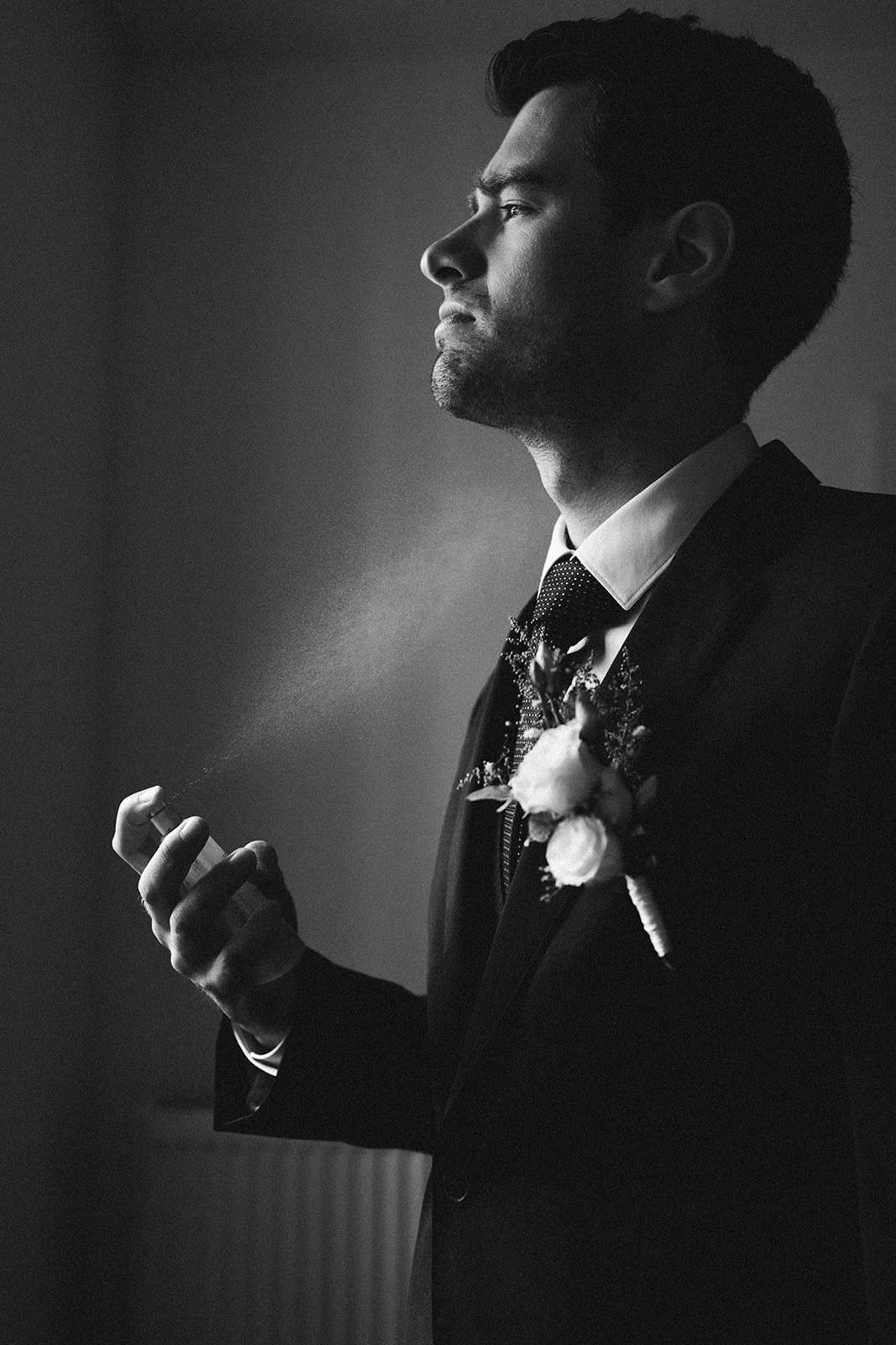 Schwarz-weiß-Foto eines Bräutigams im Anzug mit Krawatte, der Parfüm sprüht – festgehalten vom Bart van Westrop, Hochzeitsfotograf in Mainz