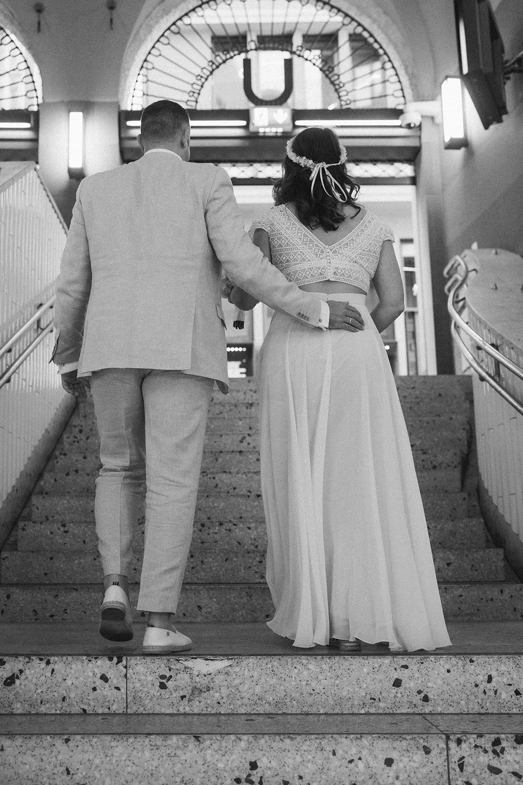Ein Paar in Hochzeitskleidung, das die Treppe hinaufgeht, im Hintergrund ein U-Bahn-Schild, in einer U-Bahn-Station. Hochzeitsfotograf Standesamt Mainz