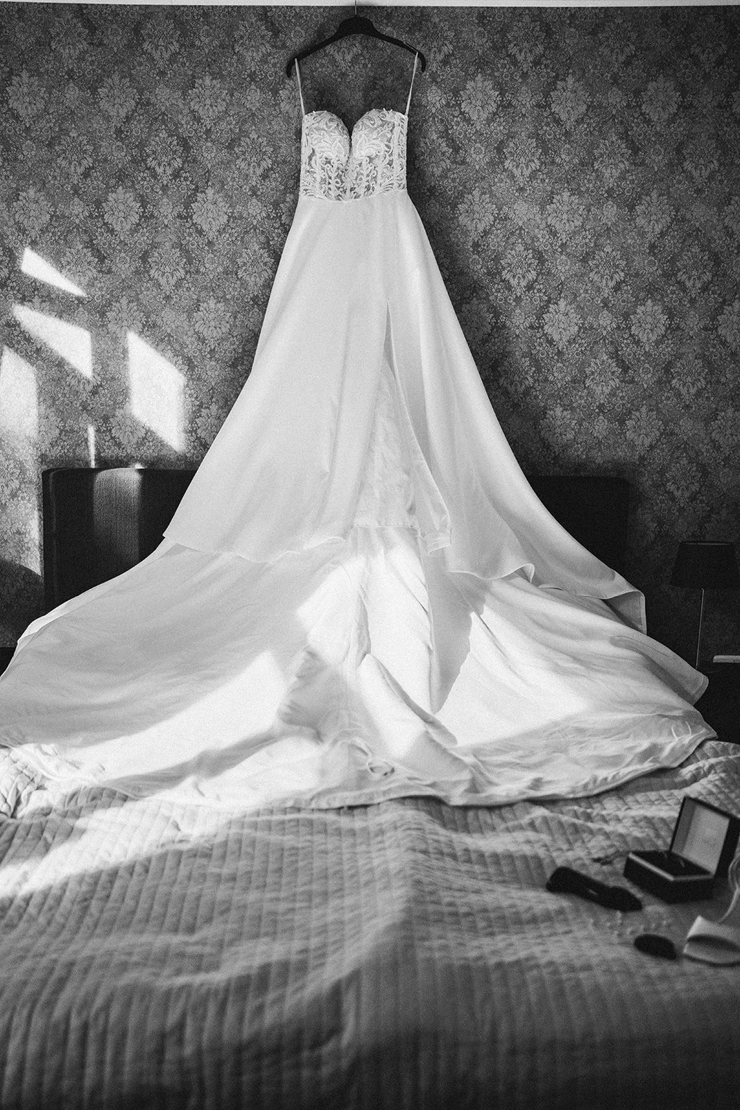 Brautkleid hängt an einer Garderobe über einem Bett mit gestreiftem Bettbezug, auf dem das Kleid teilweise liegt - festgehalten vom Bart van Westrop, Hochzeitsfotograf in Mainz