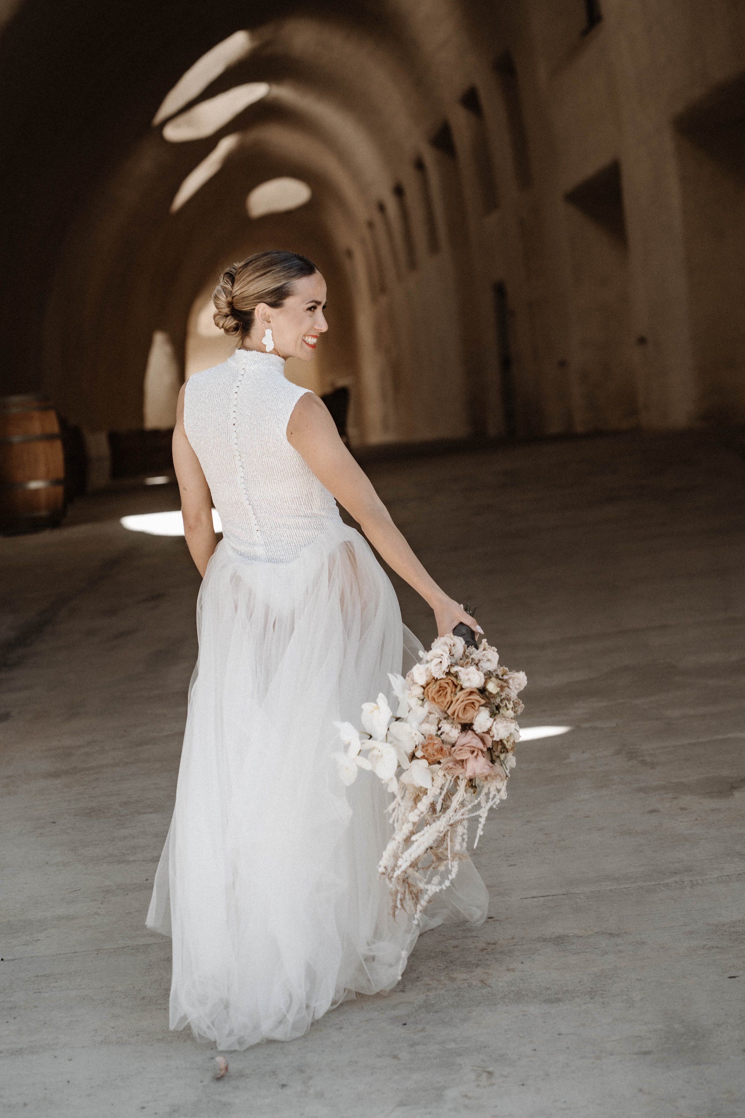 Braut hält einen Blumenstrauß in der Hand, schaut zurück und lächelt während der Hochzeit auf Mallorca – festgehalten vom Bart van Westrop, Hochzeitsfotograf in Mainz