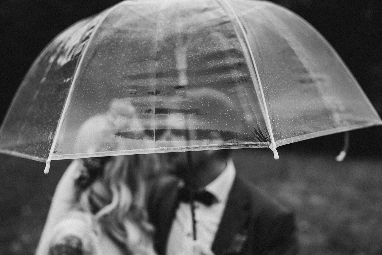 Brautpaar unter einem transparenten Regenschirm im Regen mit verschwommenem Hintergrund – festgehalten vom Bart van Westrop, Hochzeitsfotograf in Mainz