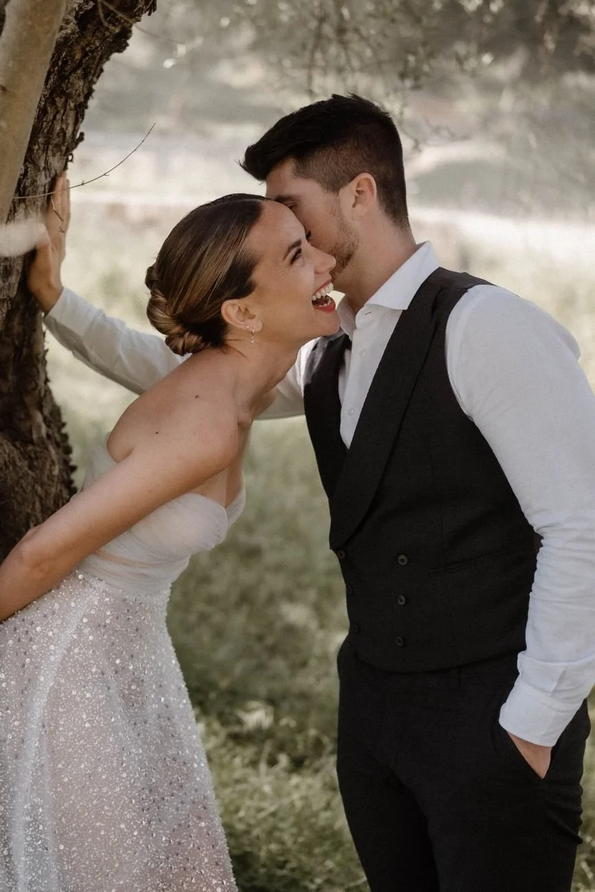 Hochzeitspaar steht lächelnd nebeneinander gegen einen Baum, in einer natürlichen und entspannten Pose, in Mallorca. Festgehalten vom Bart van Westrop, Hochzeitsfotograf in Mainz