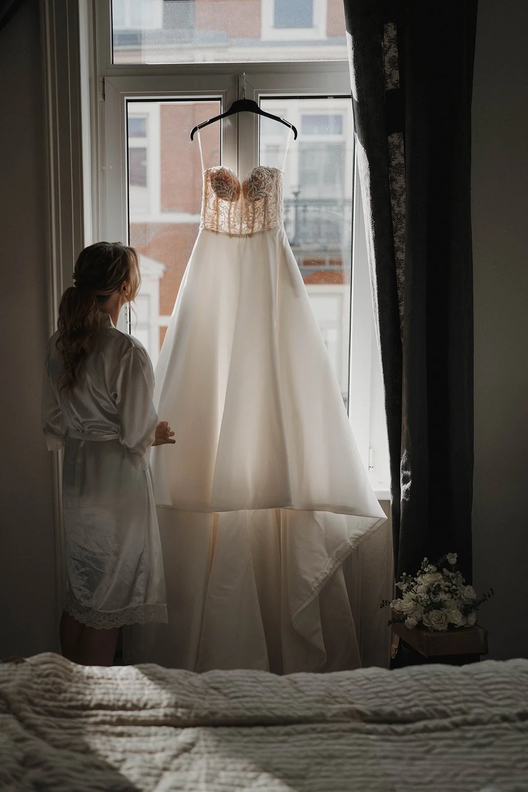 Braut schaut auf ein weißes Hochzeitskleid während des Getting Readys - festgehalten vom Bart van Westrop, Hochzeitsfotograf in Mainz