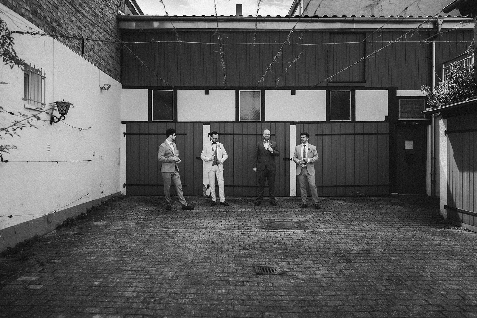 Trauzeugen in Anzügen stehen vor einer Garage während des Getting Readys – festgehalten vom Bart van Westrop, Hochzeitsfotograf in Mainz