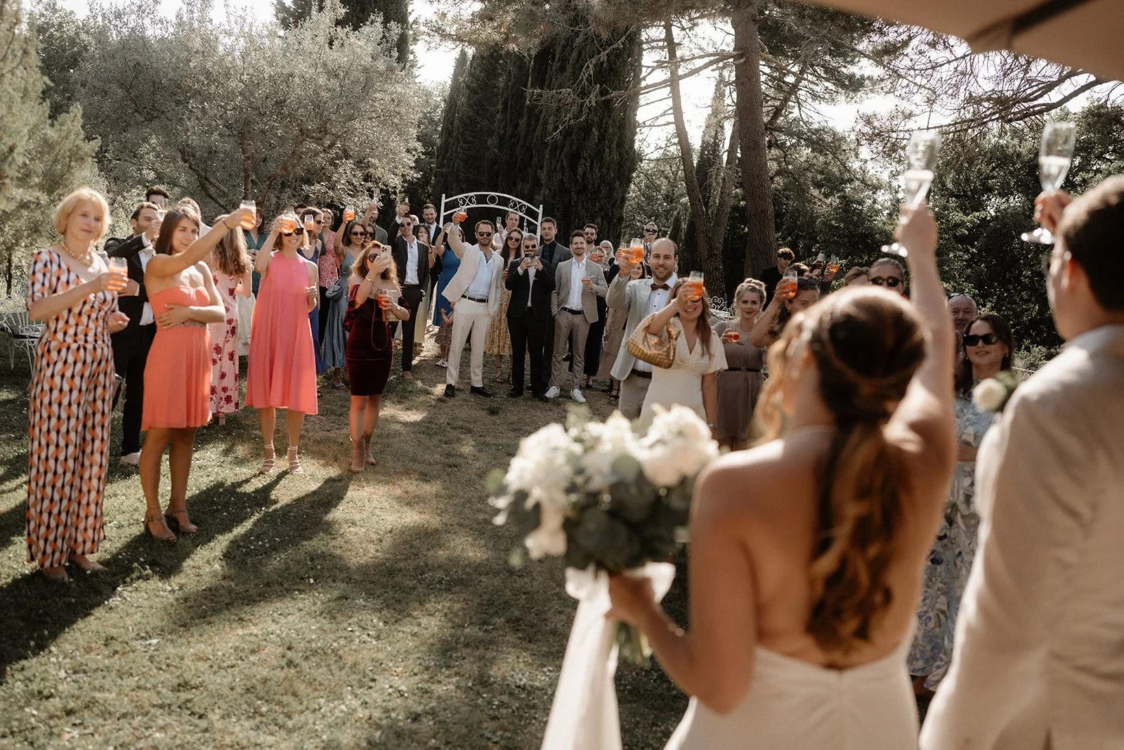 Hochzeit in der Toskana mit Braut und Bräutigam im Vordergrund, Gäste stoßen mit Gläsern an – festgehalten vom Bart van Westrop, Hochzeitsfotograf in Mainz