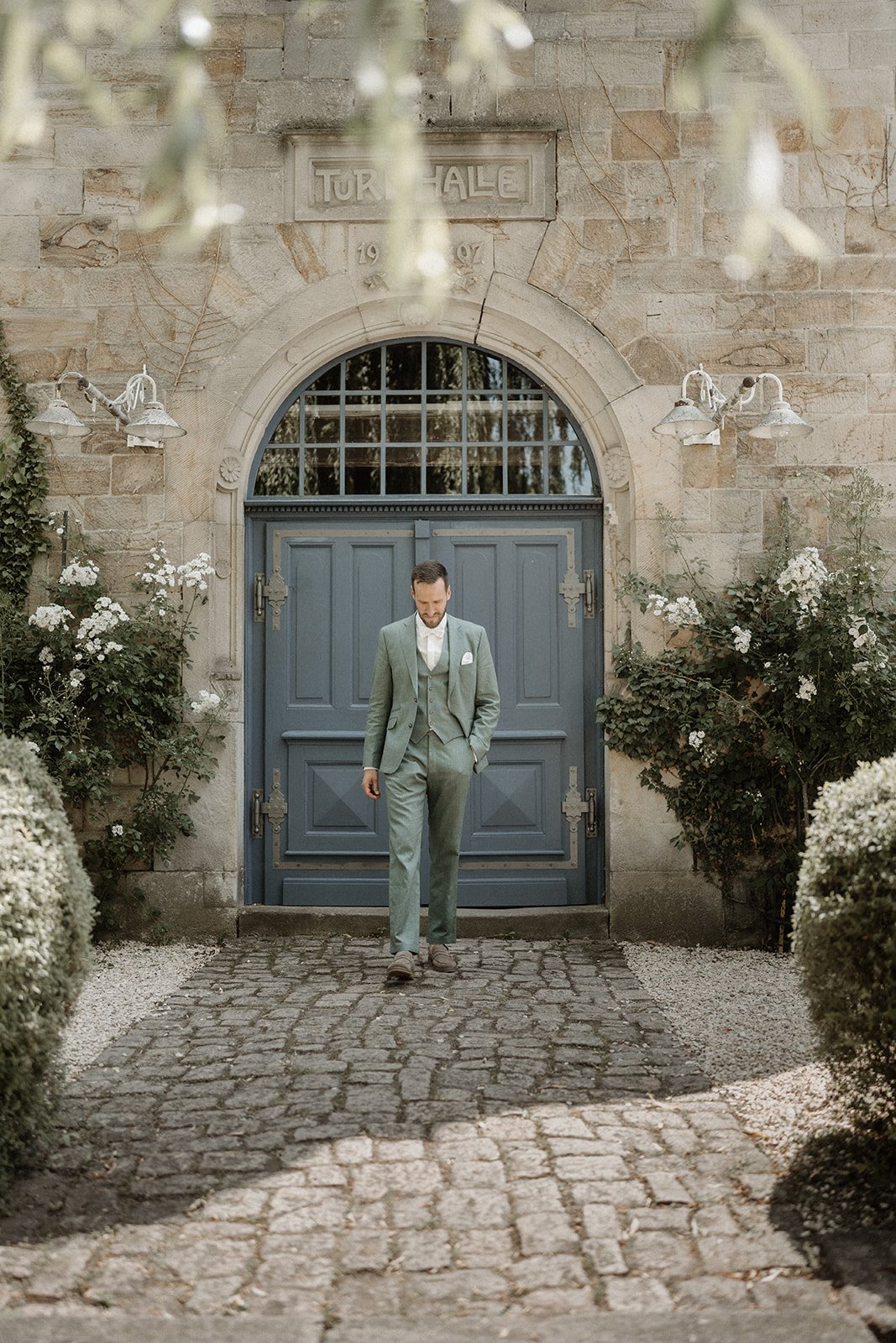 Bräutigam im Anzug läuft vor einer blauen Tür vor einer Steinfassade. Hochzeitsfotograf Wiesbaden Bart van Westrop