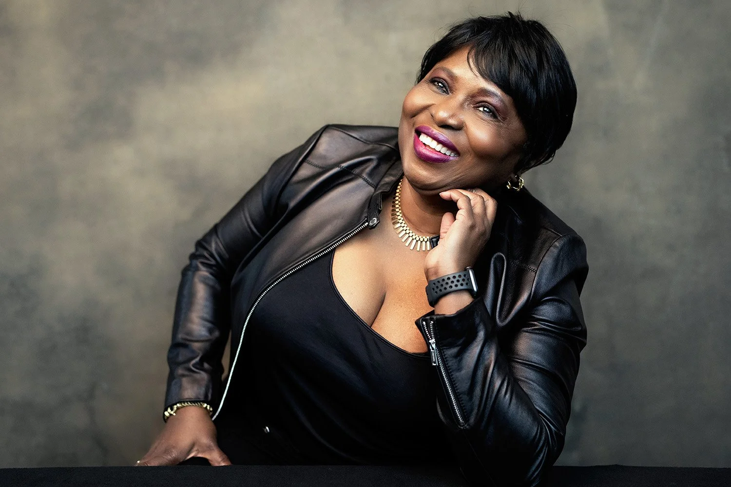 African woman sitting at table wearing a black jacket smiling.