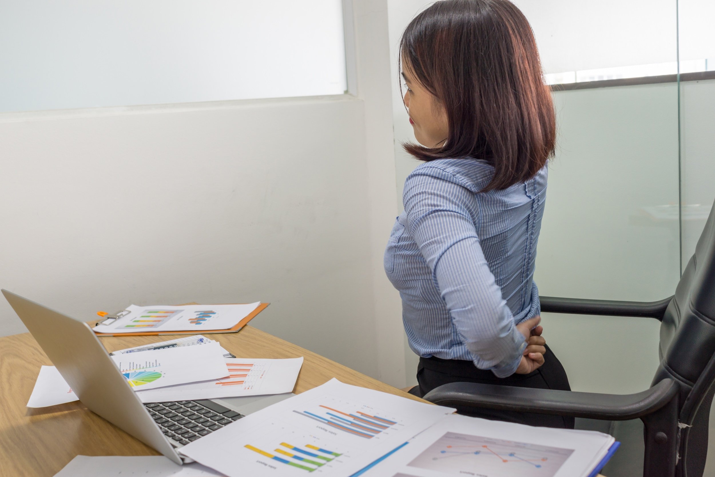 A woman in business attire at a desk stretching.