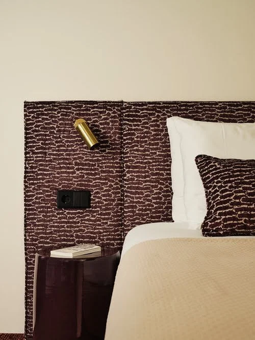 Een hotelkamer met een bed, een nachtkastje, een boek, een muur met een hoofd- en bedlamp, en een stopcontact.