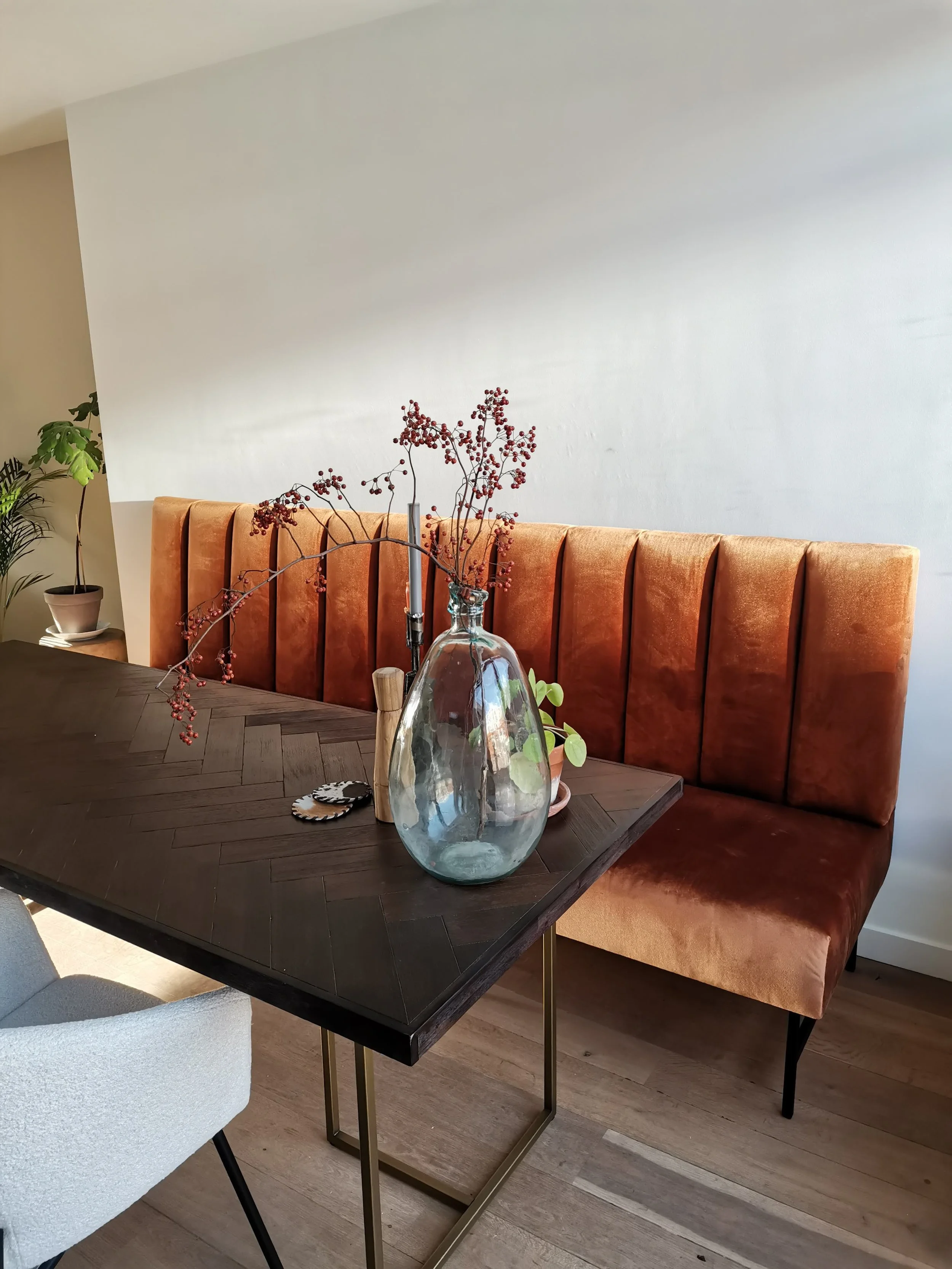 Een eettafel met een bord, een vaas met takken met rode bessen, en planten op de achtergrond.