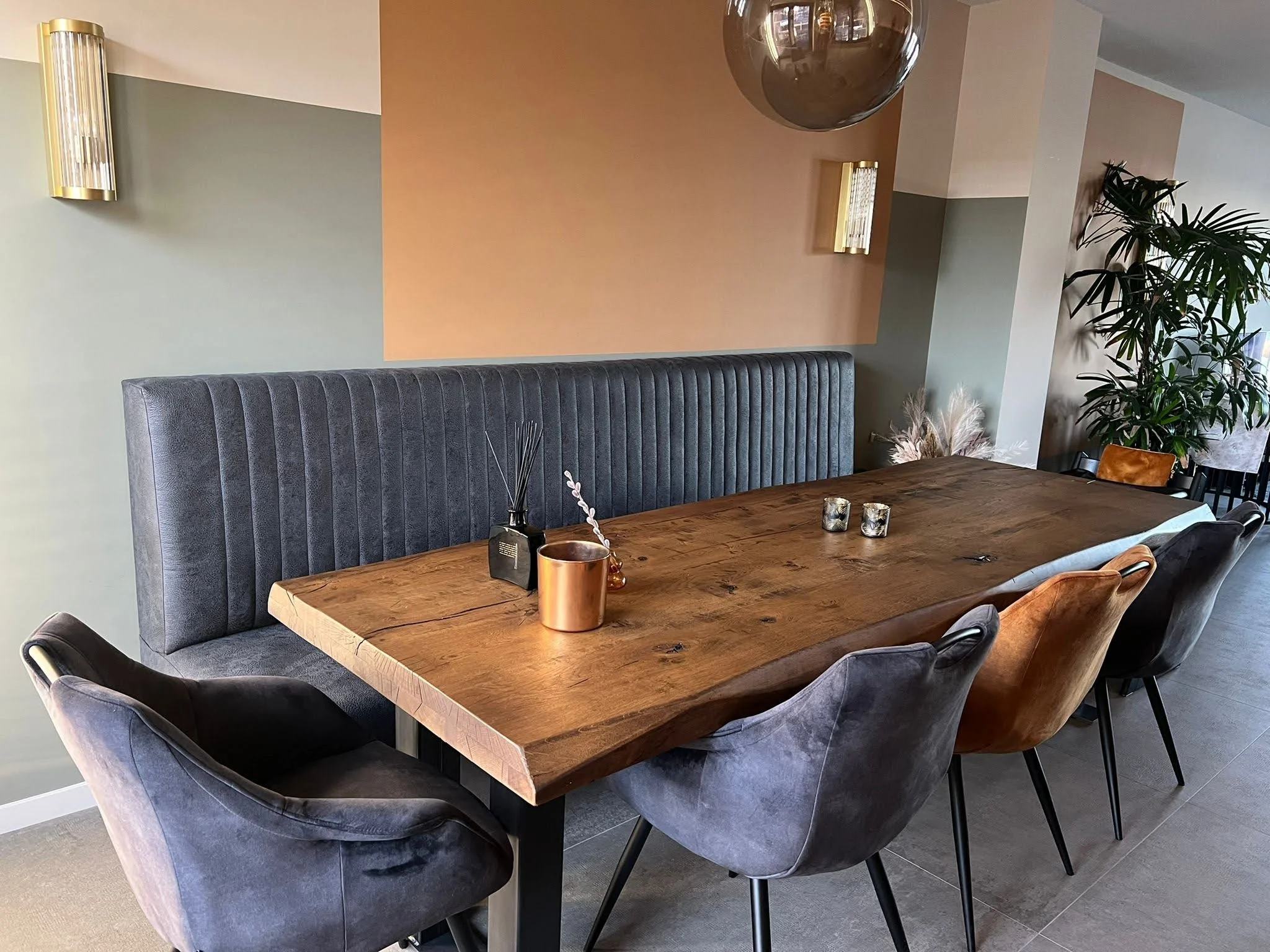 Een eetkamertafel met vier bekleedde stoelen en een bank ertegenaan, versierd met decoratieve items en kaarsen, in een modern ingerichte ruimte.