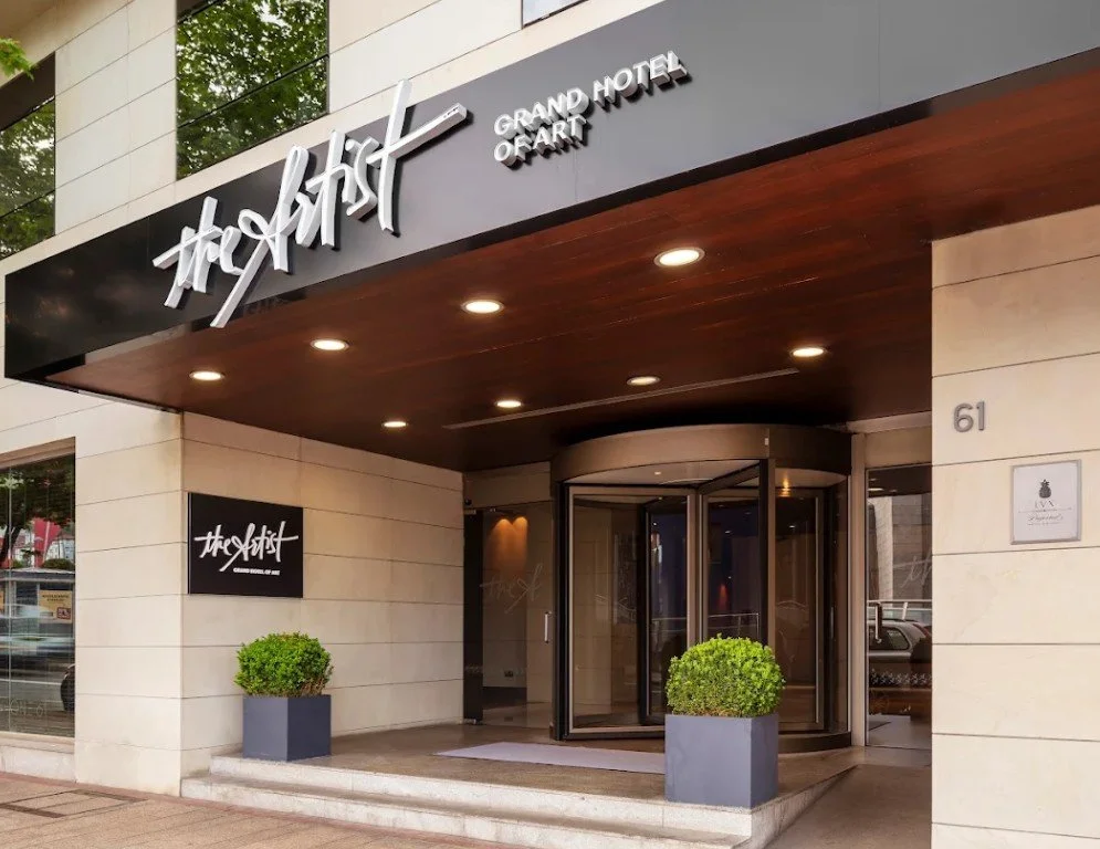 Exterior of a hotel entrance with a revolving door, modern signage, and potted plants.