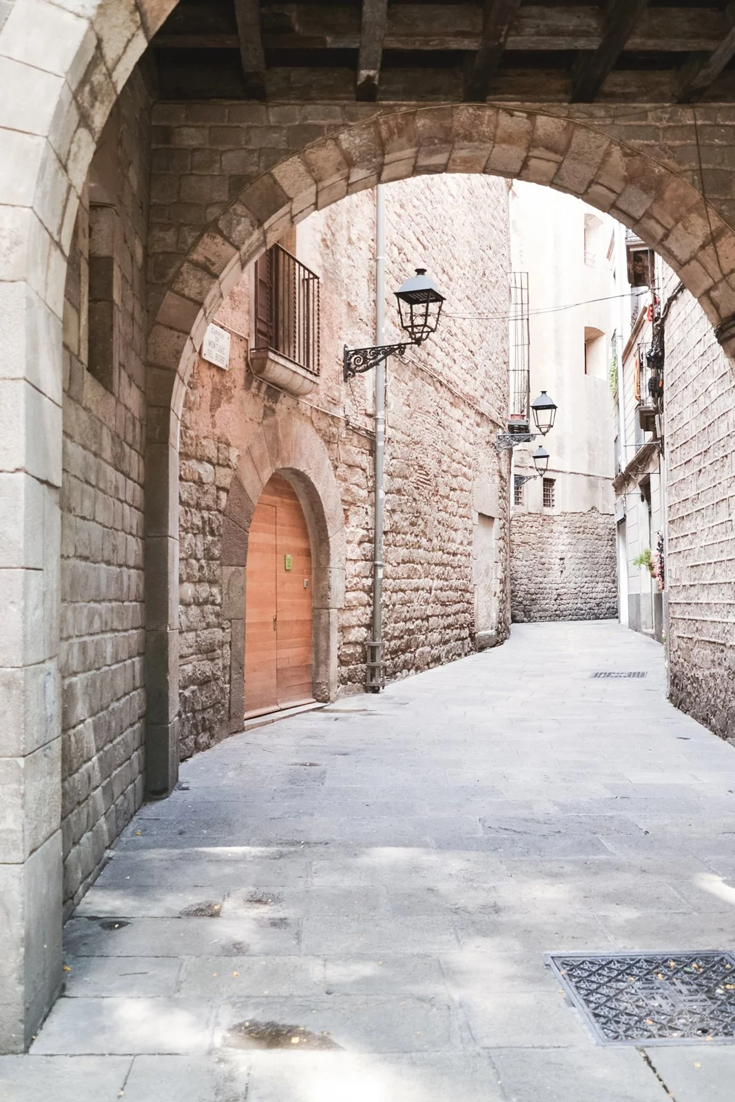 A narrow, old stone alleyway with arch overhead, brick walls, and vintage street lamps.