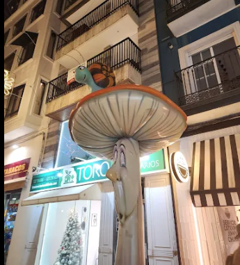 Decorative street scene with a large mushroom-shaped structure featuring a cartoon mouse figure on top, and a building with balconies in the background.