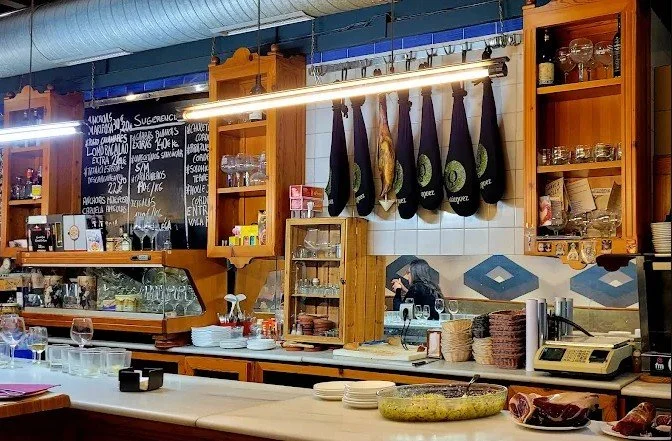 Interior of a restaurant or bar with hanging black aprons, shelves with glassware, and a counter with plates and a phone.