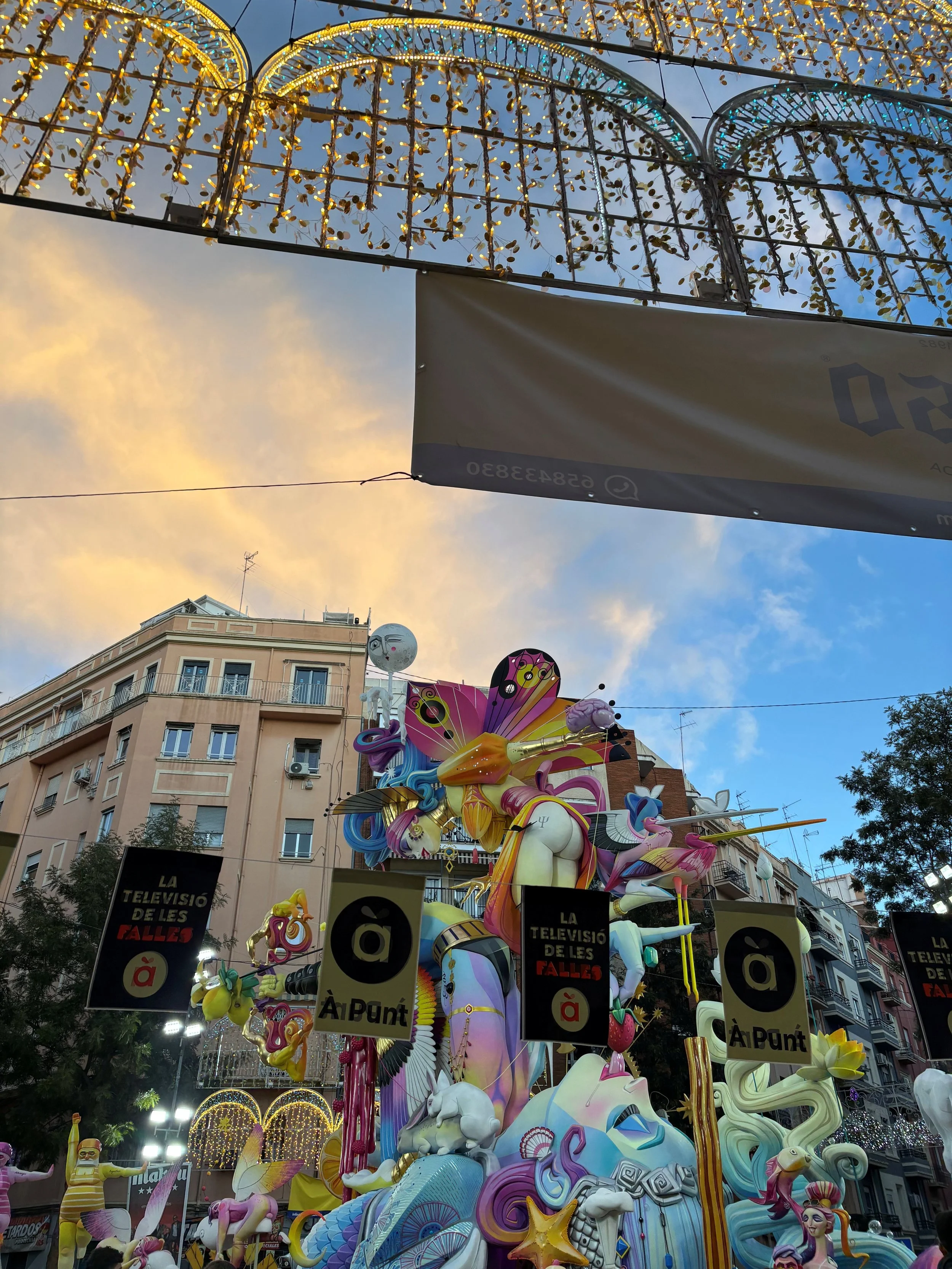 Colorful carnival or parade float featuring fantasy characters such as unicorns, mermaids, and other mythical creatures, with decorated buildings and festive lights in the background.