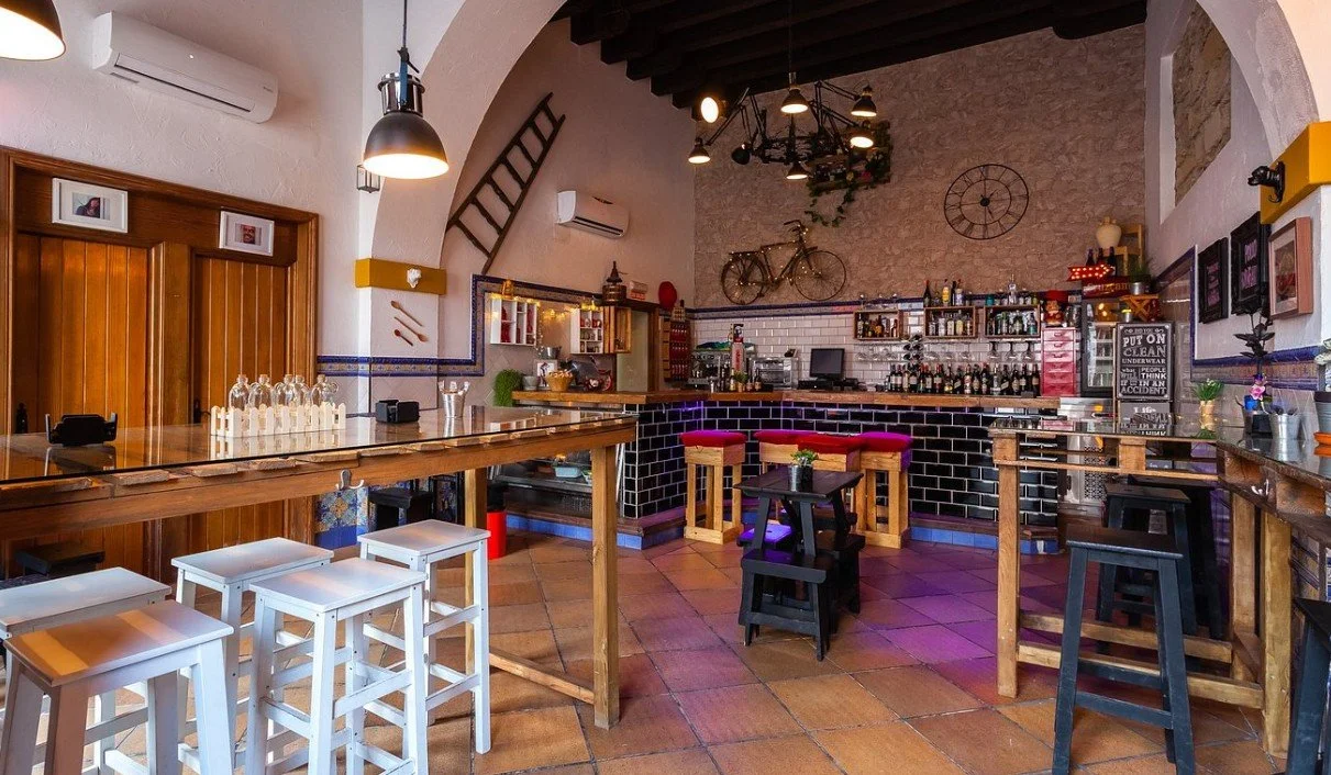 Interior of a cozy bar with wooden furniture, black tiled bar counter, and various decorations like a bicycle and clock on the wall.