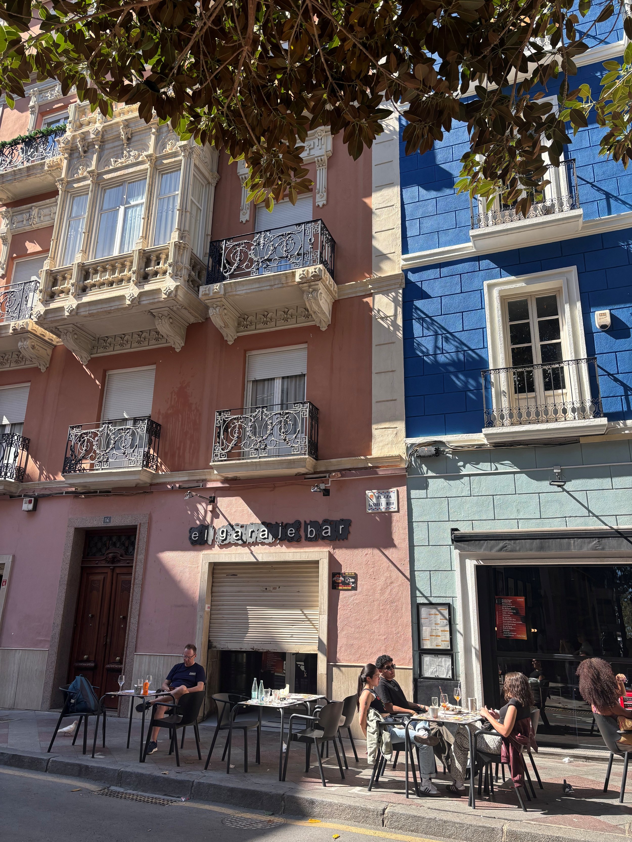 People dining outside a restaurant on a city street, with colorful buildings and outdoor seating.