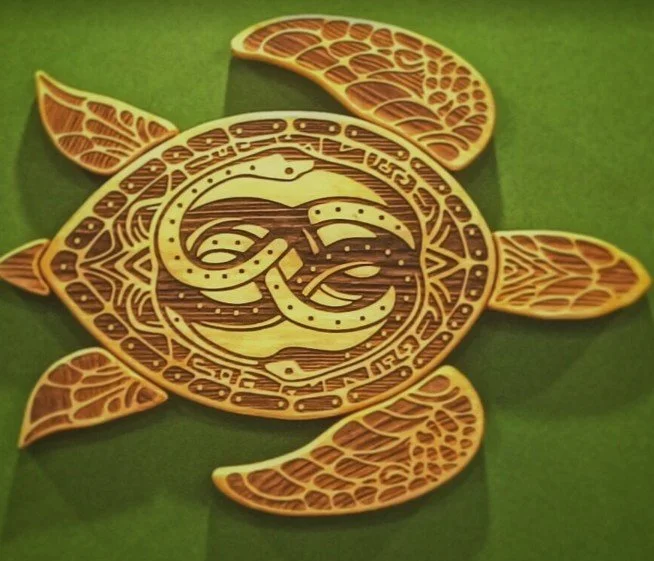 Decorative wooden turtle with intricate cut-out patterns, surrounded by four carved orange slices, placed on a green background.