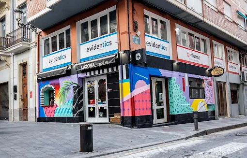 Corner building with colorful mural art, signage for 'evidentics' and 'tainforma,' and storefront windows in an urban setting.