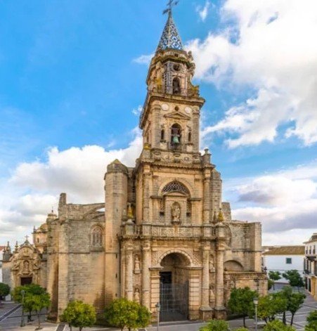 Historic stone church with tall bell tower and ornate spire, set against a partly cloudy blue sky.