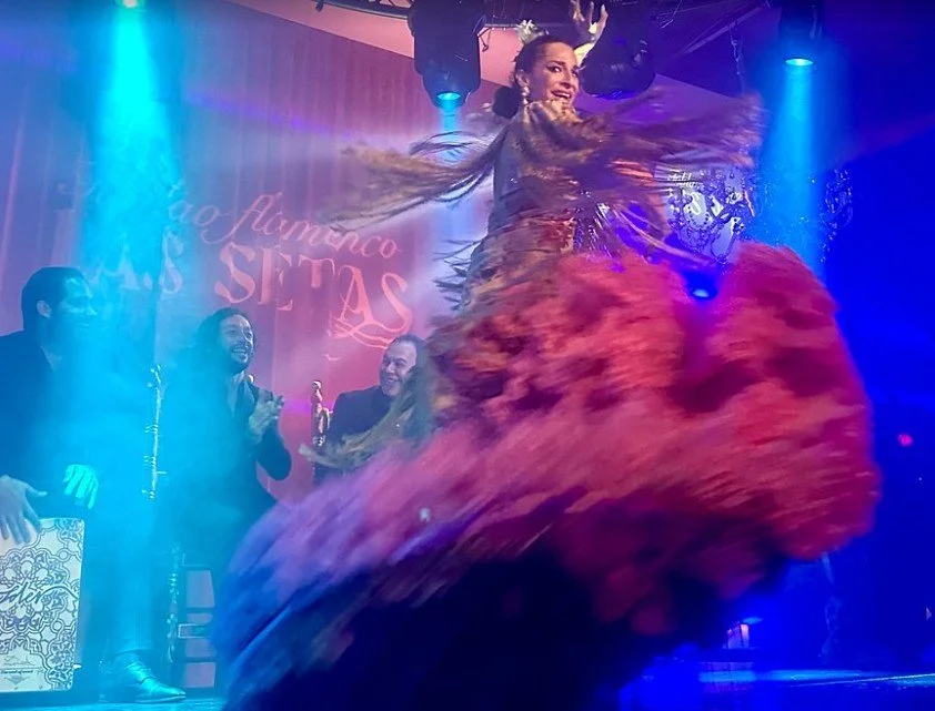 Flamenco dancer performing on stage with three musicians in the background, colorful stage lighting, and a sign that reads "Flamenco Las Setas".