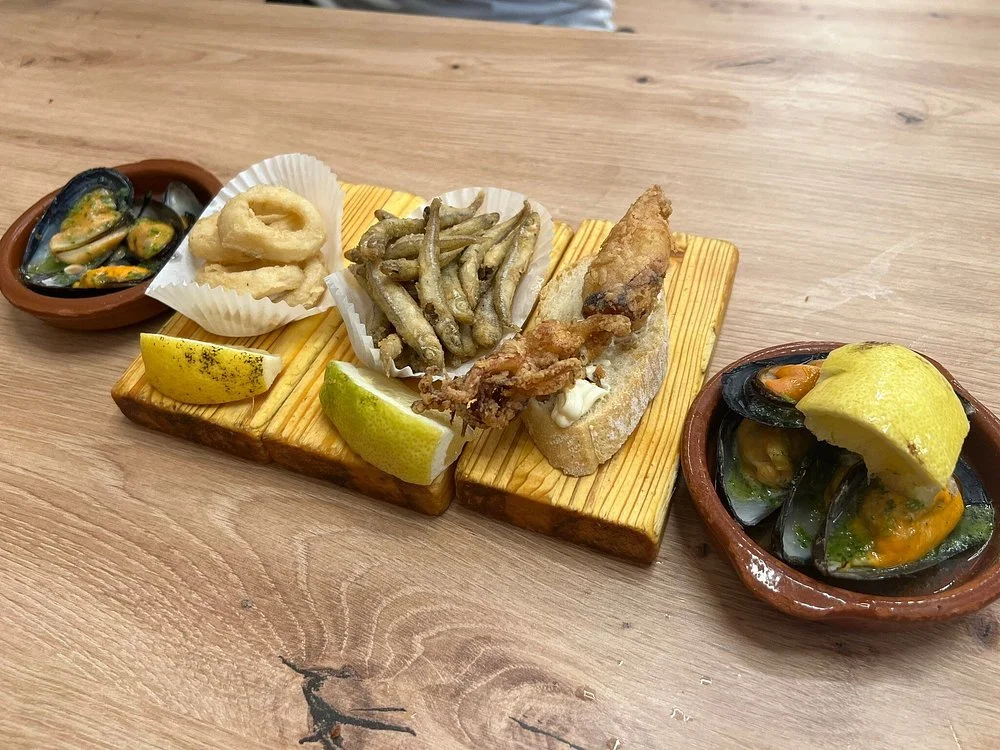Plate with fried fish, fried calamari, fried small fish, lemon wedges, and two bowls of mussels in broth with lemon wedges.