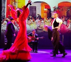 A flamenco dancer in a red dress performing on stage with an audience and musicians in the background.