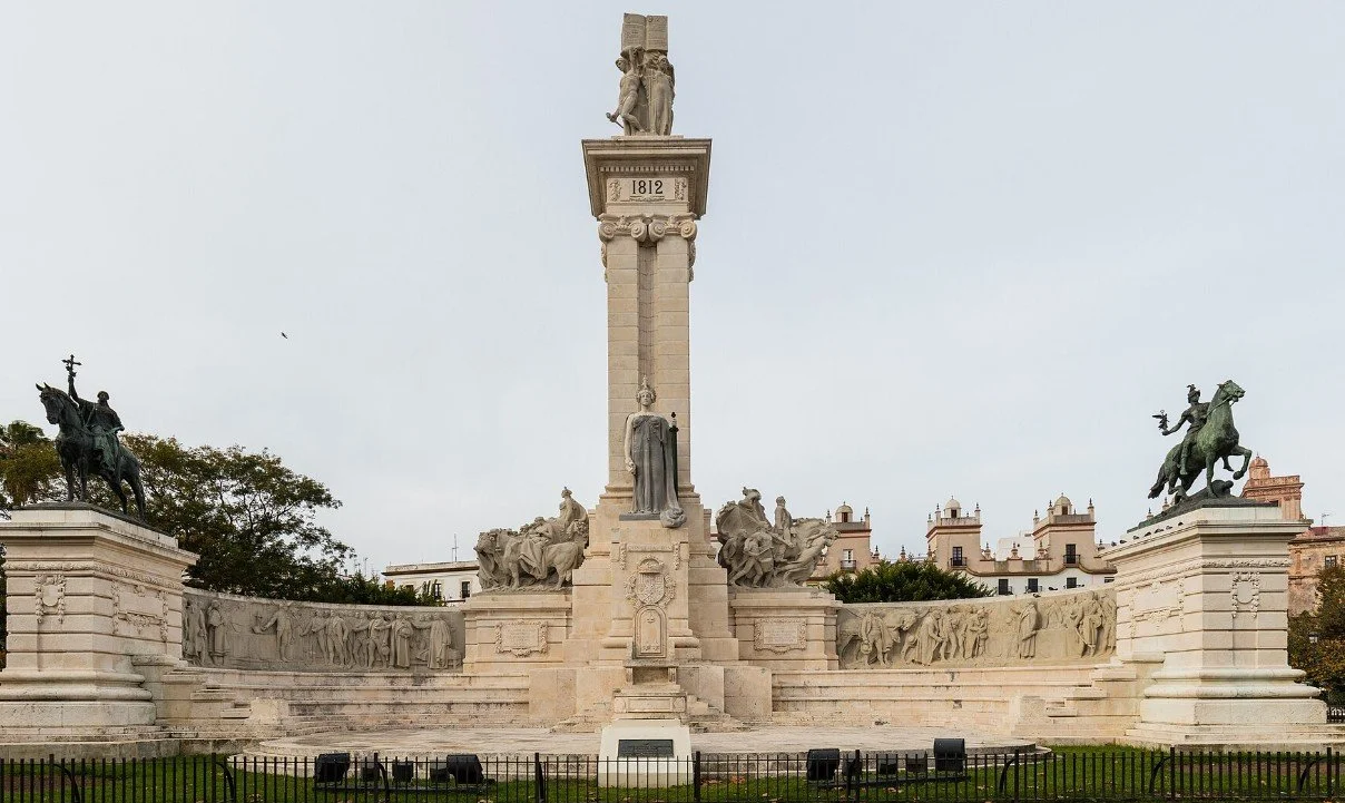 A large historical monument featuring statues and sculptures, with a central column topped by a statue and two equestrian statues on either side.