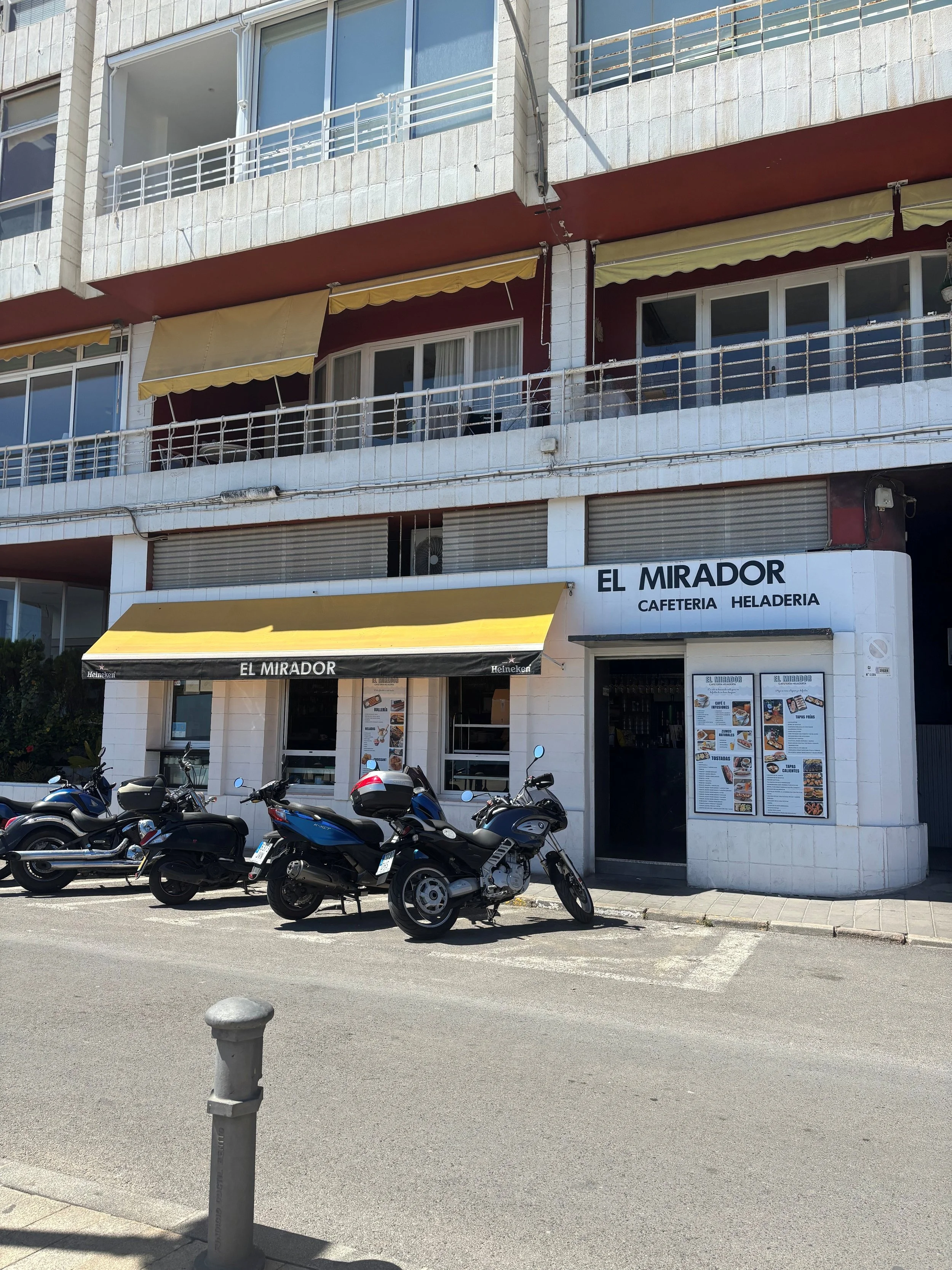 A building with a restaurant on the ground floor named 'El Mirador' offering cafeteria and ice cream, with motorcycles parked in front of the entrance.