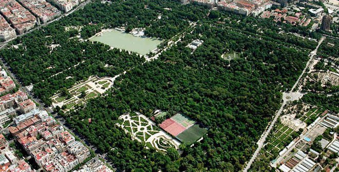 Aerial view of a large lush green park with winding pathways, a sports field, and surrounding city streets.