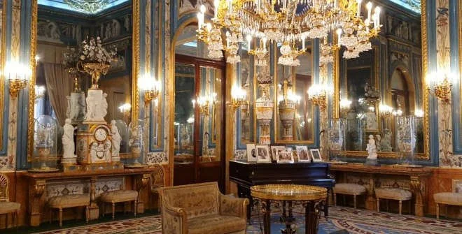 Elegant living room with ornate gold and blue decor, large mirrors, chandeliers, and classical sculptures.