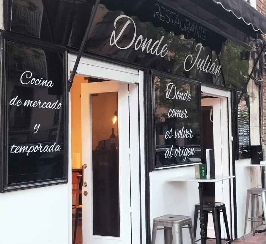 Exterior of a restaurant called 'Donde Julián' with black signs displaying its name and menu descriptions in Spanish.