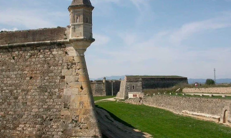 Historic stone fortress with thick walls, battlements, and watchtowers under a blue sky.