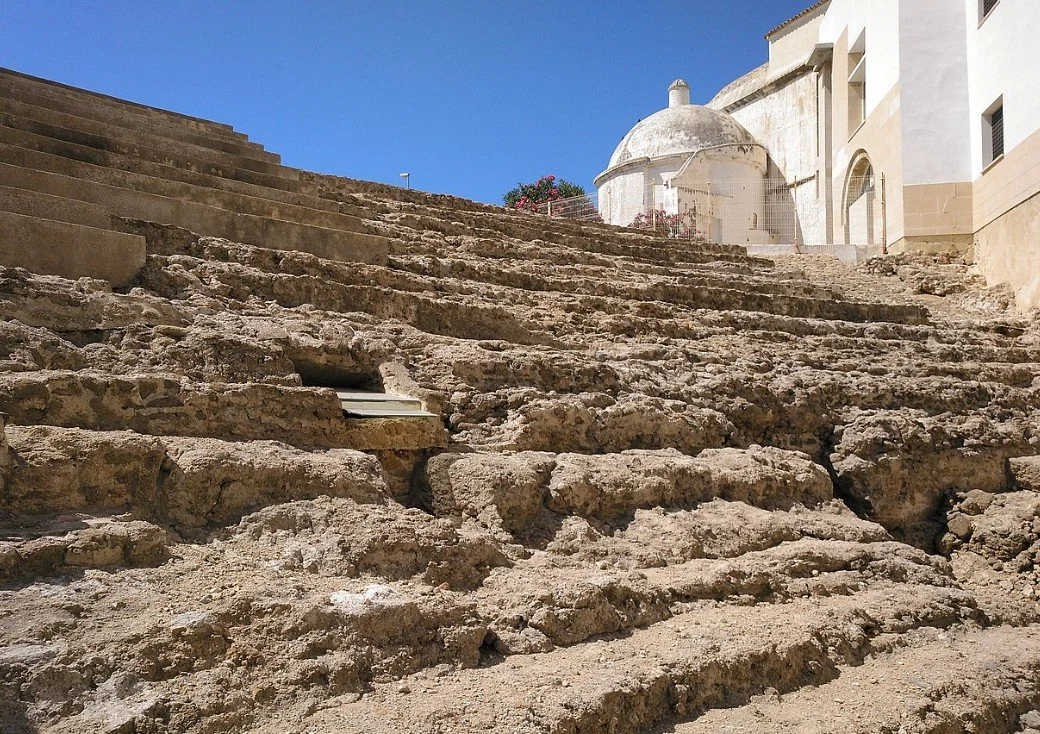 Worn stone steps leading up to a white circular building with a dome, part of a historic site under a clear blue sky.