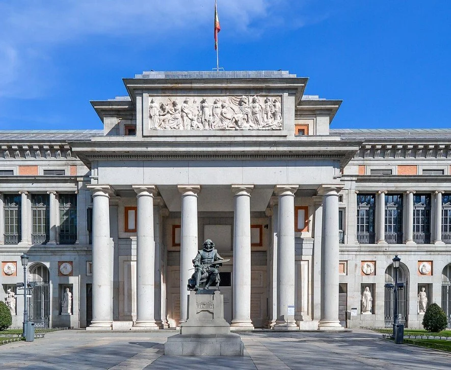Federal Reserve building with classical architecture, flanked by statues, with an American flag on top, under a blue sky.