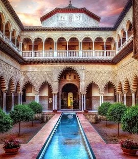Interior view of a traditional courtyard with a central water fountain, surrounded by intricately decorated arched walkways and lush greenery.