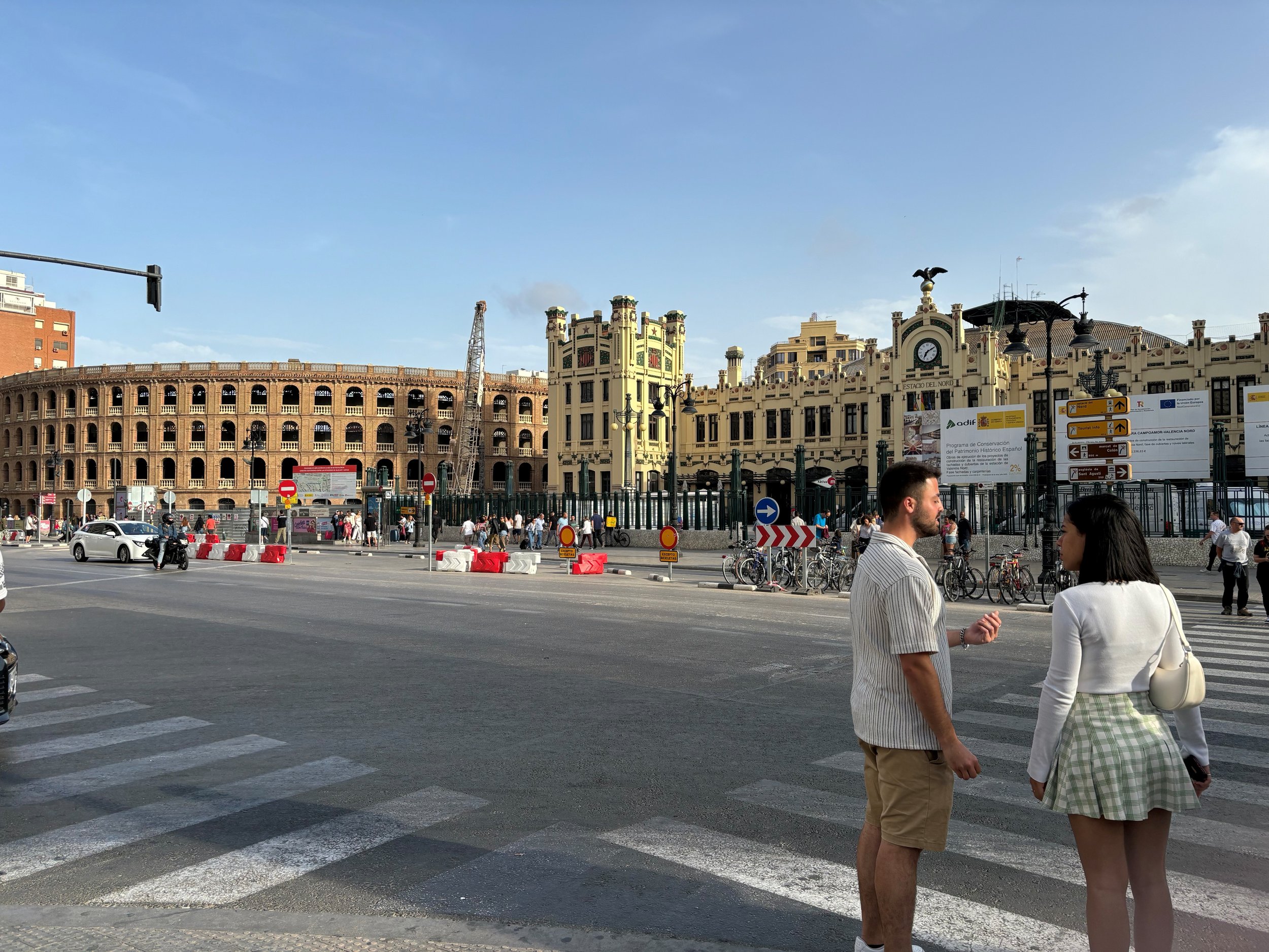 People crossing a street with historic buildings, a crane, and blue sky in the background.