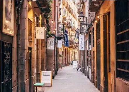 A narrow alleyway in an urban area with cafes and shops on both sides, string lights above, and signage advertising different places.