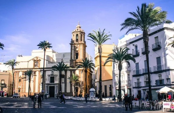 City square with historic church, palm trees, and people walking and gathering.