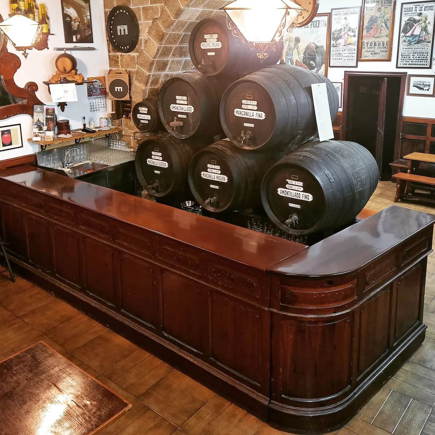 A bar area in a restaurant with large black wine barrels stacked on top of a wooden counter, surrounded by framed posters and photographs.