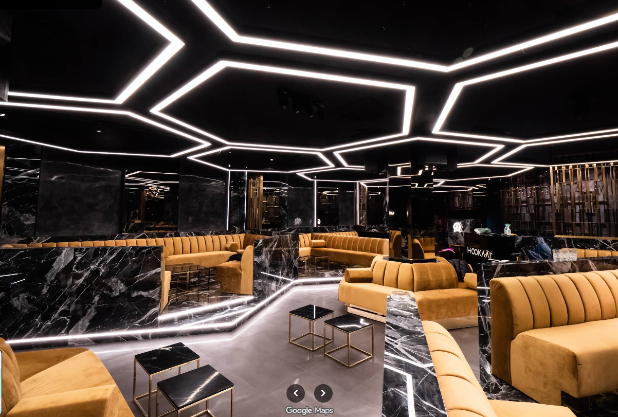 A modern lounge with black marble walls and gold accents, featuring mustard-colored velvet seating and geometric LED ceiling lighting.