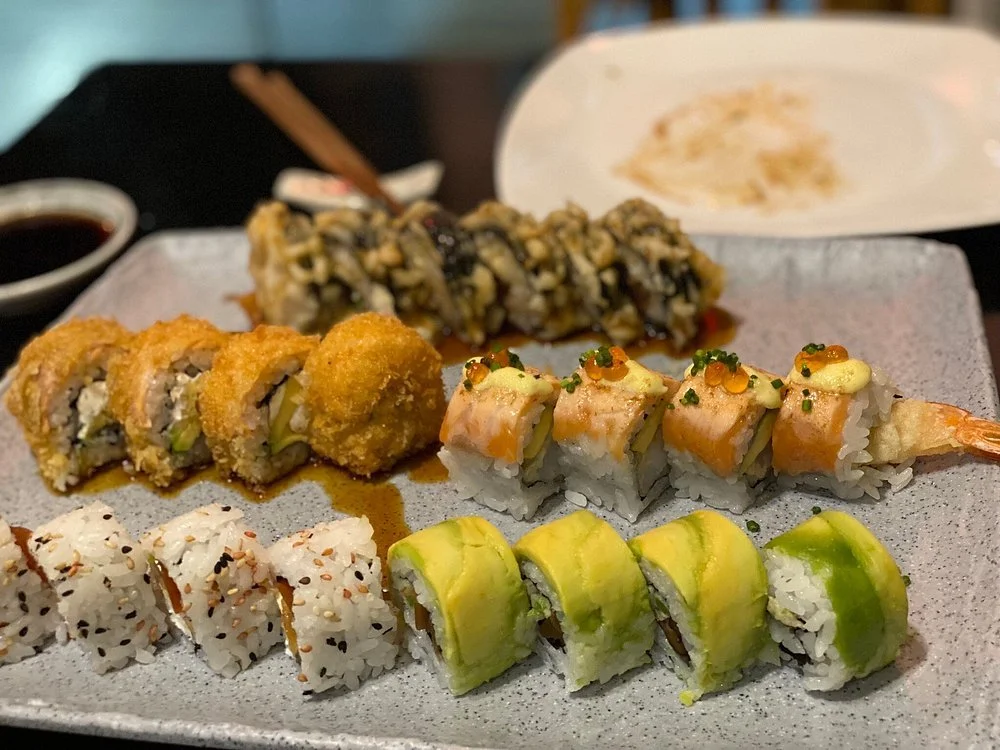 Assorted sushi rolls on a plate with soy sauce in the background.