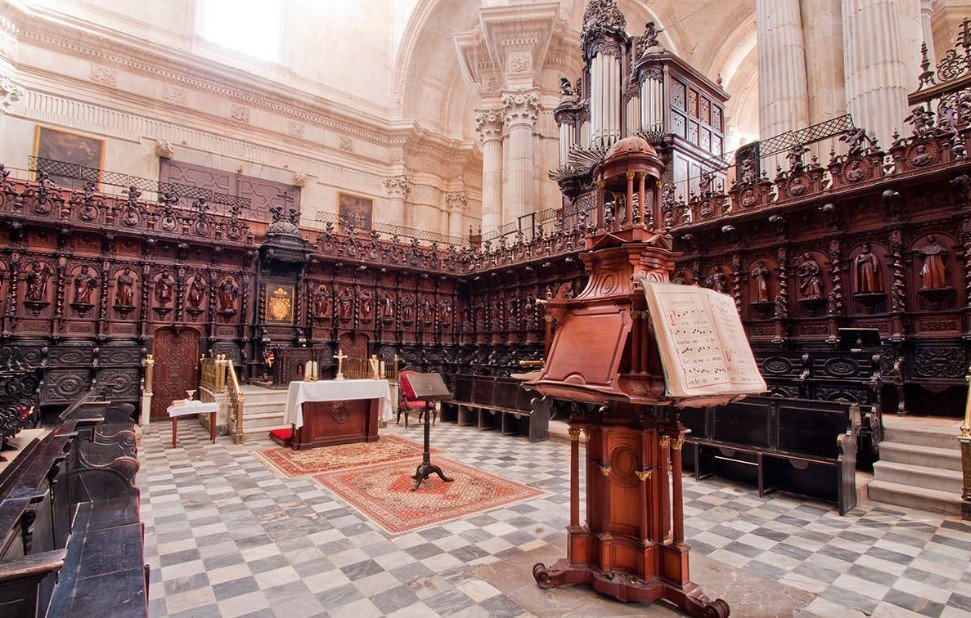 An ornate church interior with dark wooden pews, a pulpit with sheet music, and a small altar with candles and a red chair.