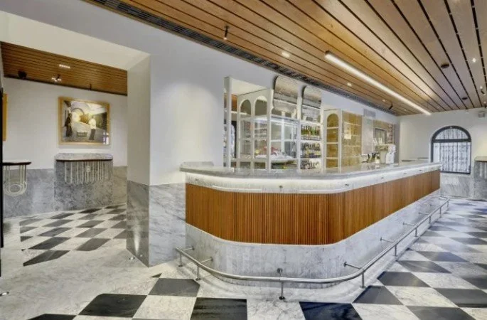 Modern interior of a bar or reception area with a curved counter, marble flooring with black and white checkered pattern, and wooden ceiling panels.