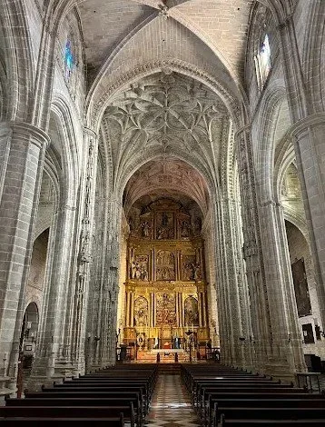 Interior of a historic church with tall vaulted ceilings, stone arches, and an ornate gold altar at the front.
