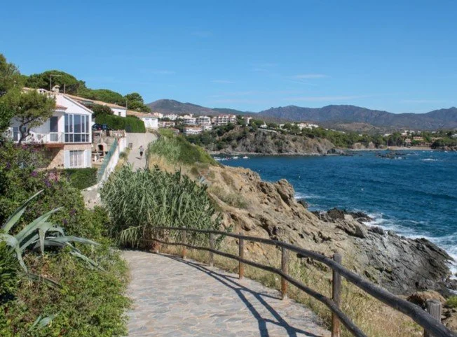 Scenic coastal pathway with rocks, ocean, and houses along the hillside