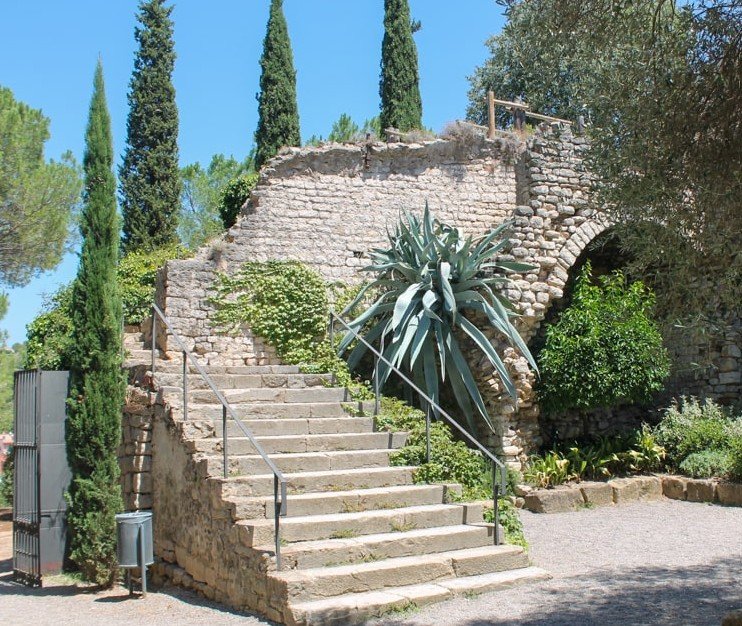 Stone staircase leading up to an ancient stone wall with greenery and cypress trees in the background.