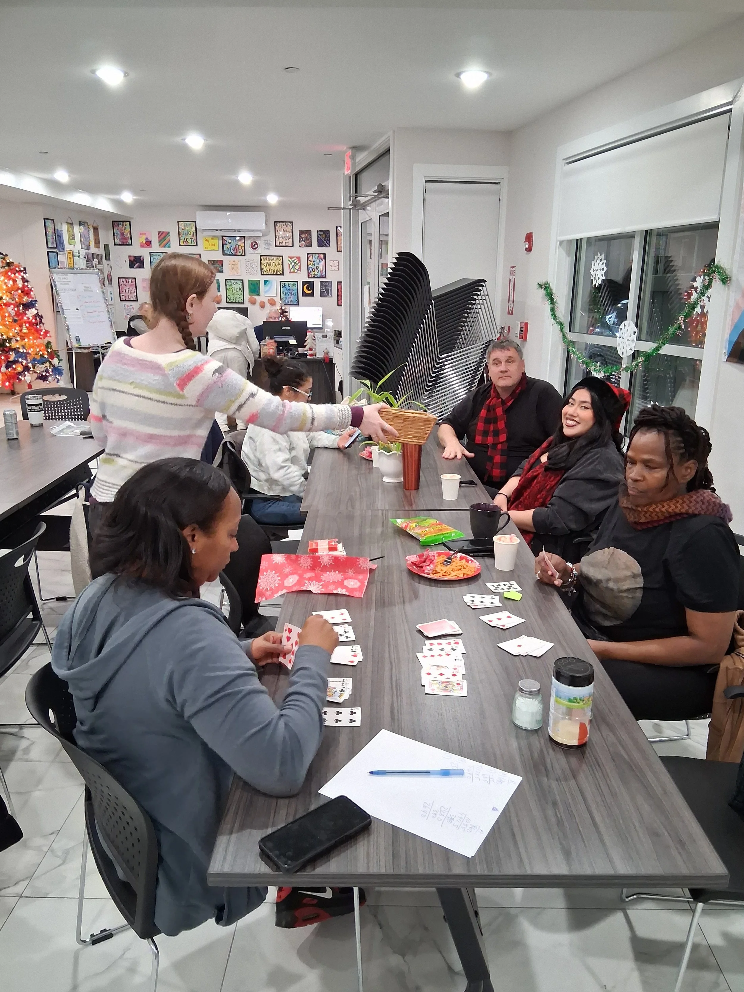 Group of people playing cards around a table decorated for Christmas, with a Christmas tree and Christmas decorations in the room.