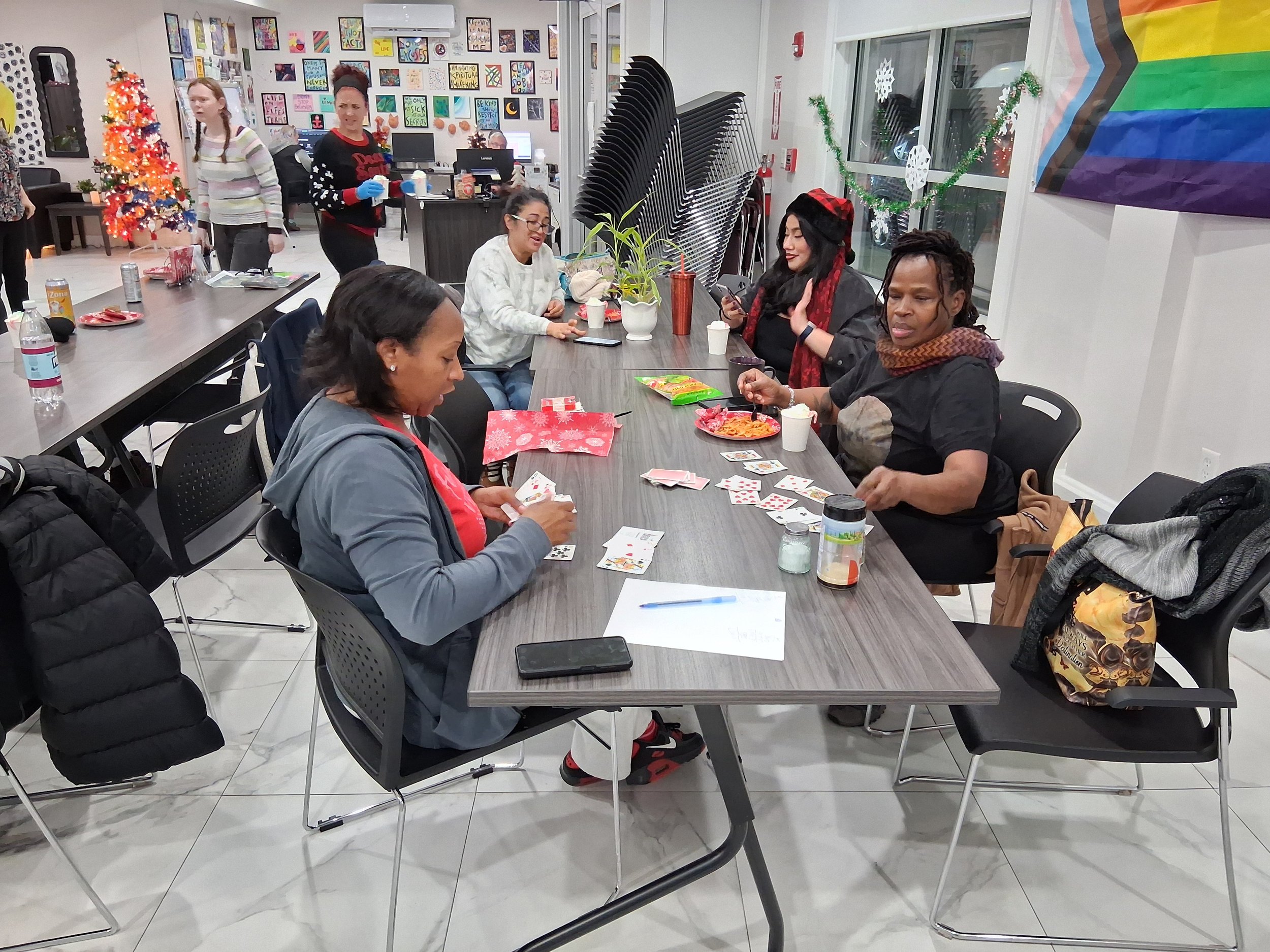 Group of women sitting around a long table playing a card game, Christmas decorations including a Christmas tree and presents in the background